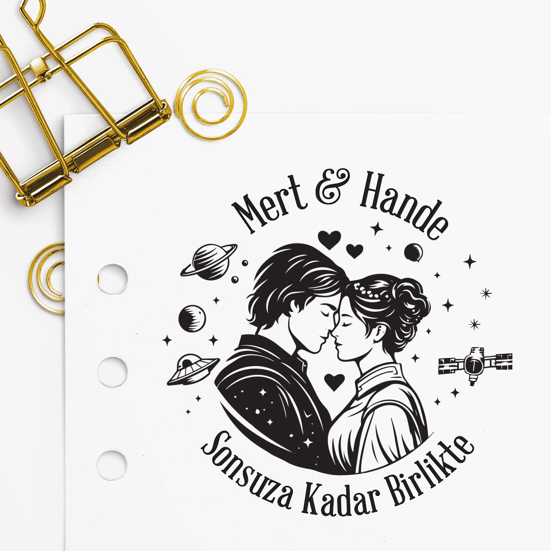 Alınlarını birbirine deyen çift figürlü, halkalı gezegen, uzay gemisi ve yıldız detaylarıyla galaksi temalı kitap mührü tasarımı, 'Mert & Hande' isim örneğiyle